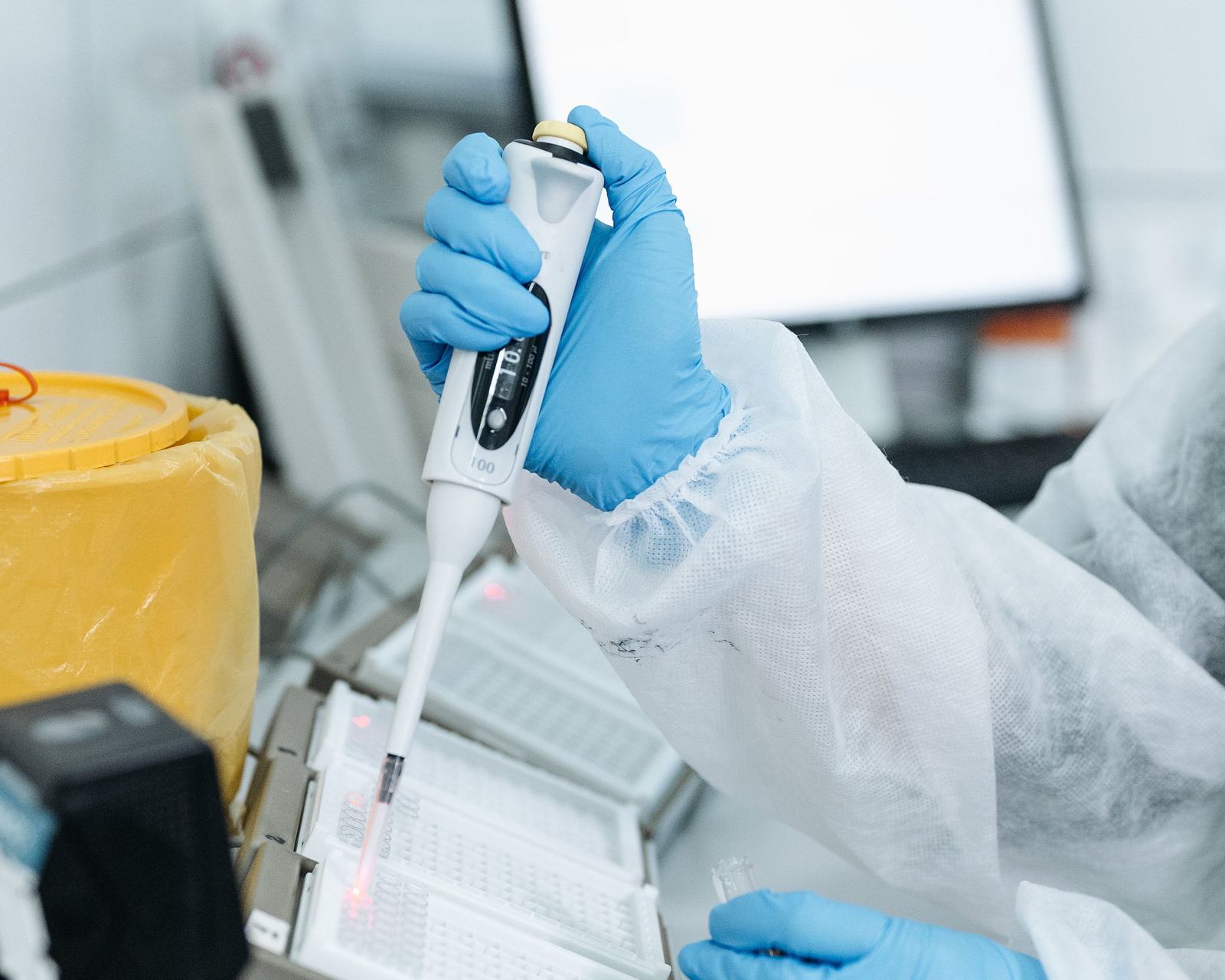 A gloved laboratory technician pipetting into a plate at a diagnostics bench, with lot and label-printing cards from Odoo floating above