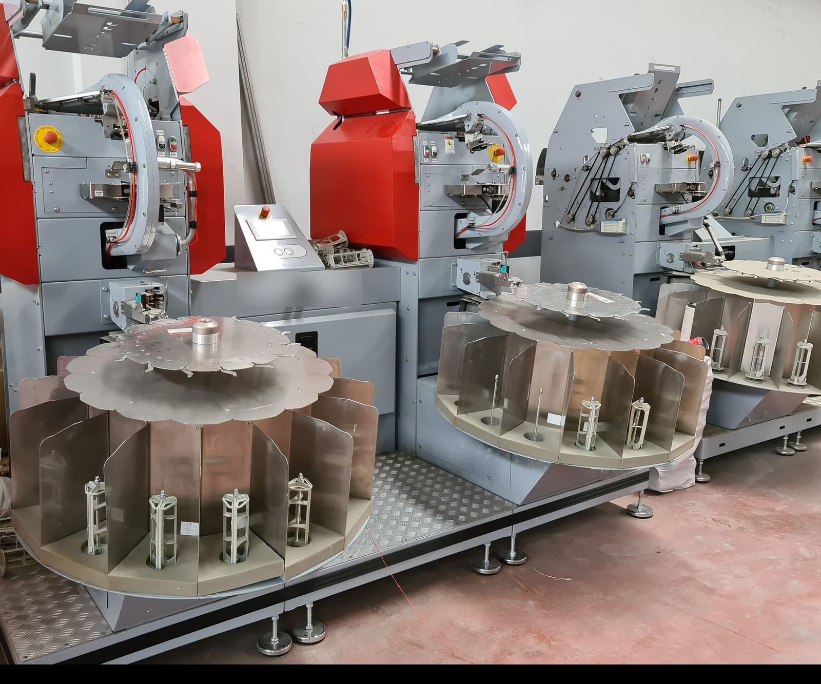 A row of red and grey filling machines on a production floor, with planning and quality cards from Odoo floating above